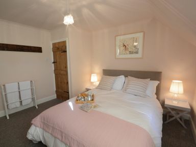A bedroom with a bed with striped pillows and a pink blanket with lamps on bedside tables at 2 The Dunes Thorpeness