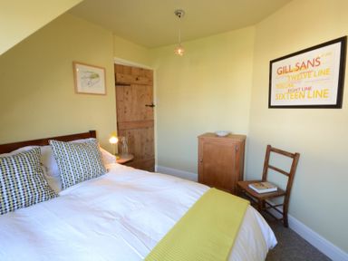 A bedroom with a bed pillows a yellow throw a wooden door a small cabinet and a chair at 2 The Dunes Thorpeness