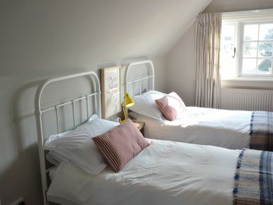 A bedroom with two single beds with white metal headboards and striped pillows at 2 The Dunes Thorpeness