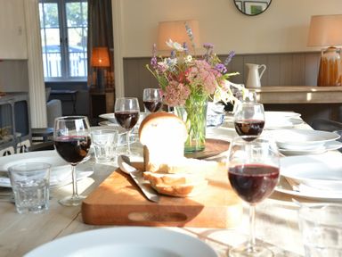 A dining table set with glasses of red wine white plates a loaf of bread on a cutting board and a vase of flowers at 2 The Dunes Thorpeness