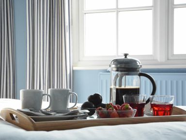 A tray with coffee cups a coffee press strawberries and glasses on a bed near a window at 2 The Dunes Thorpeness