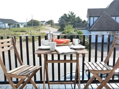 A balcony with a wooden table set for two with cups plates a coffee pot and watermelon at 2 The Dunes Thorpeness