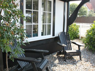 Two wooden chairs on a gravel patio outside a house with a white window and black trim at 2 The Dunes Thorpeness