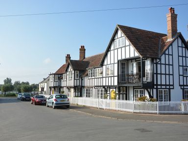 A street with cars parked outside Tudor-style houses with white picket fences at 2 The Dunes Thorpeness
