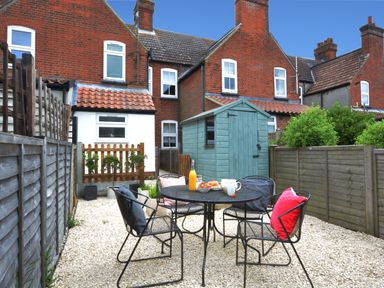 A backyard patio with a black metal table and four chairs with cushions and a wooden shed at Holmleigh Aldeburgh