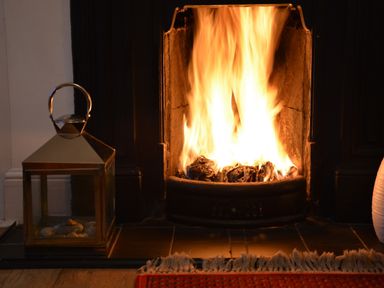A burning fireplace with a lantern on the hearth and part of a red rug at Holmleigh Aldeburgh