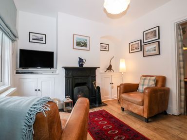 A living room with two brown leather armchairs a red patterned rug a black fireplace a television on a white cabinet and framed pictures on the walls at Holmleigh Aldeburgh in Aldeburgh