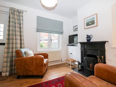 A sitting room with two brown leather armchairs a window with a blue roman blind a black fireplace with a blue jug on the mantle and a television on a white cabinet at Holmleigh Aldeburgh in Aldeburgh