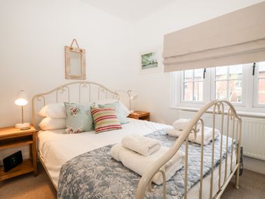 A bedroom with a metal bed frame two wooden bedside tables with lamps and stacked towels on the bed at Holmleigh Aldeburgh in Aldeburgh