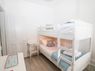 A bedroom with a white bunk bed a small white side table and a white door at Holmleigh Aldeburgh in Aldeburgh