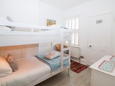 A bedroom with white bunk beds a wicker chair a window with shutters and a small white dresser at Holmleigh Aldeburgh