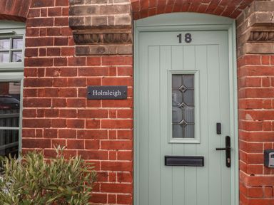 A green front door with the number 18 and a name plaque reading Holmleigh on a red brick wall at Holmleigh Aldeburgh