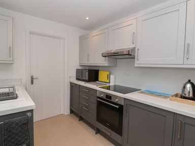 A kitchen with grey and white cabinets a microwave oven a built in oven stovetop kettle and a dish rack at Holmleigh Aldeburgh