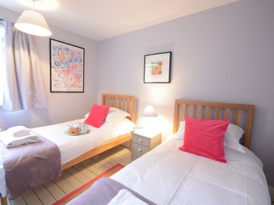 A bedroom with two single beds with pink pillows a bedside table a lamp and two framed pictures on the wall at Durdans Walberswick