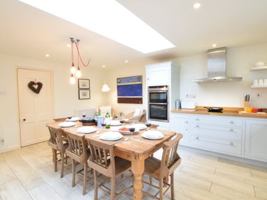 A kitchen with a wooden dining table and chairs set with plates and glasses at Durdans Walberswick