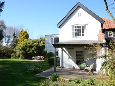 A garden with a patio, wooden chairs, a table, and a white house at Durdans Walberswick