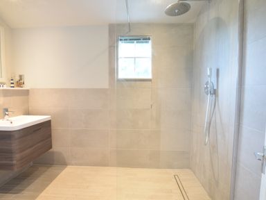 A bathroom with a walk-in shower a window a wall-mounted sink and gray tiles at Durdans Walberswick in Walberswick