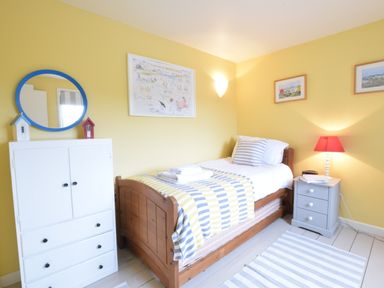 A bedroom with a single wooden bed a white cabinet with a round mirror and a gray nightstand with a red lamp at Durdans Walberswick