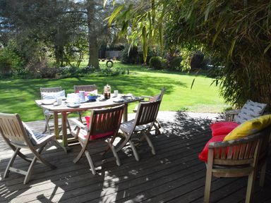 An outdoor wooden deck with a table and chairs set for dining overlooking a garden at Durdans Walberswick in Walberswick