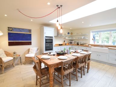 A kitchen with a wooden dining table set for six with wine glasses and plates at Durdans Walberswick