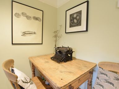 A wooden table with a vintage typewriter between two chairs against a wall with framed art at Durdans Walberswick in Walberswick