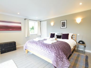 A bedroom with a double bed covered with a purple quilt and purple pillows beside a window at Durdans Walberswick