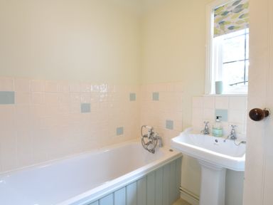 A bathroom with a bathtub, pedestal sink, tiled walls, and a window at Durdans Walberswick