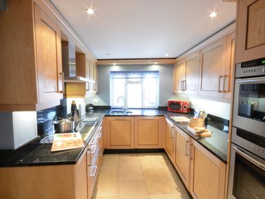 A kitchen with wooden cabinets black countertops and cooking appliances at Bunny Cottage Aldeburgh