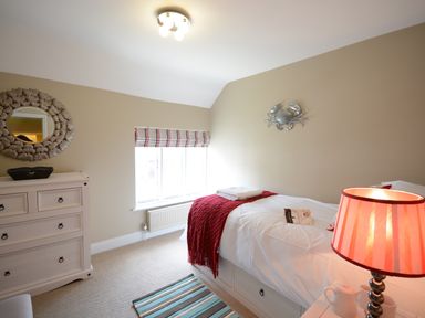 A bedroom with a single bed covered with white bedding and a red throw at Bunny Cottage Aldeburgh