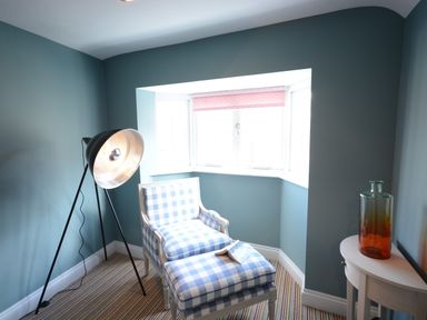 A room with a blue checkered armchair and footstool next to a large floor lamp and a console table with a glass bottle at Bunny Cottage Aldeburgh