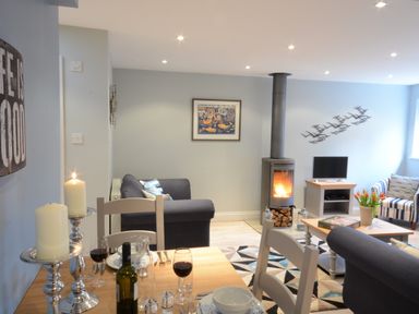 A living room with a dining table set with wine and candles a wood stove and a television at Bunny Cottage Aldeburgh