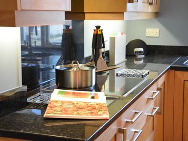 A kitchen countertop with a stainless steel pot on a stovetop and a cookbook open at Bunny Cottage Aldeburgh