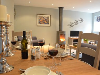 A dining table set with wine glasses and silver candle holders in a living room with a wood stove and TV at Bunny Cottage Aldeburgh