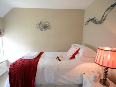 A single bed with white linens and a red blanket in a bedroom with a bedside table and lamp at Bunny Cottage Aldeburgh