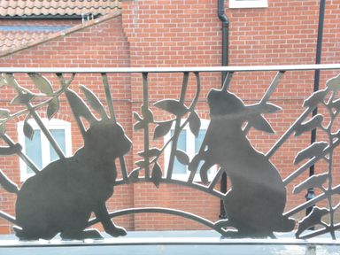 A metal railing with silhouettes of two rabbits and leaves against a brick building