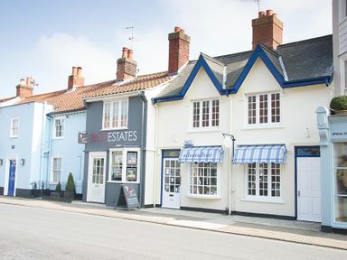 A street view of buildings with an estate agent and a shop with striped awnings at Bunny Cottage Aldeburgh