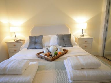 A bedroom with a bed having two grey pillows two bedside tables with lamps and folded towels at Red Robin  Whepstead in Wickhambrook near Bury St Edmunds