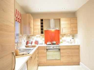 A kitchen with wooden cabinets a sink with a cutting board and bread a stove with pots and a red backsplash at Red Robin Whepstead in Wickhambrook near Bury St Edmunds