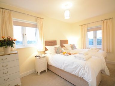 A bedroom with two single beds a bedside table with a lamp and windows with curtains at Red Robin Whepstead in Wickhambrook near Bury St Edmunds
