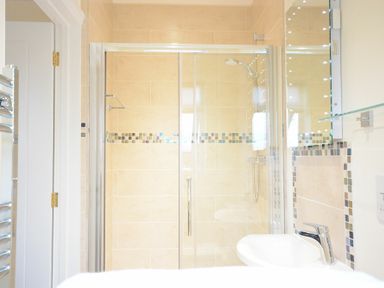 A bathroom with a glass shower enclosure a shower head a white sink and a wall mirror at Red Robin Whepstead in Wickhambrook near Bury St Edmunds