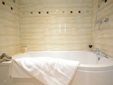 A bathroom with a bathtub featuring a white towel a glass of red wine small bottles of bath products and a magazine at Red Robin Whepstead in Wickhambrook near Bury St Edmunds