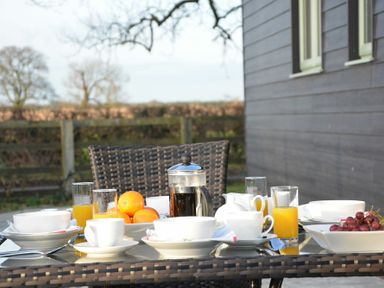 An outdoor dining table with cups glasses of orange juice a bowl of oranges a bowl of grapes and a coffee press at Red Robin Whepstead in Wickhambrook near Bury St Edmunds