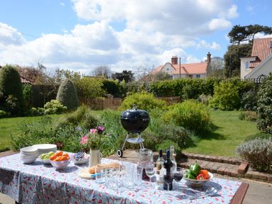 A garden with a table set for a meal with plates glasses bottles and bowls of fruit and vegetables at Holly Lodge in Aldeburgh