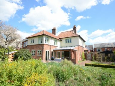 A two story house with red brick lower walls and cream upper walls with a garden in front at Holly Lodge in Aldeburgh