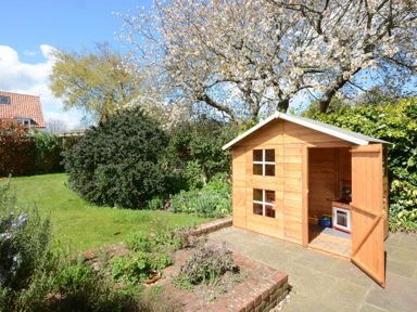 A garden with a wooden playhouse with an open door and a small flower bed at Holly Lodge in Aldeburgh