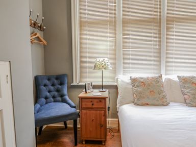 A bedroom with a chair, nightstand, lamp, and bed at Holly Lodge in Aldeburgh