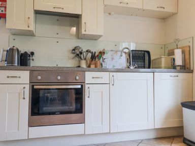 A kitchen with white cabinets a built-in oven a kettle and utensils on the countertop at Romulus in Larling near East Harling