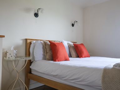 A bedroom with a wooden bed frame and white bedding with orange and beige cushions at Romulus Larling near East Harling