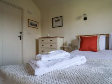 A bedroom with a bed with white towels and a red pillow a chest of drawers and framed pictures on the wall at Romulus in Larling near East Harling