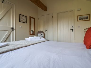 A bedroom with a bed towel and red cushion a wooden door a chair with a cushion and wall artworks at Romulus Larling near East Harling